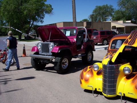 1972 Ford Ranchero - Two custom vehicles, a pink Jeep and a yellow hot rod, are displayed outdoors at an event.