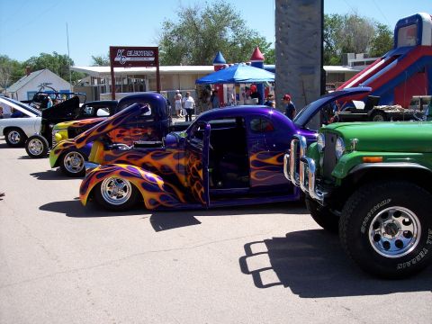 1972 Ford Ranchero - A line of custom vehicles, including a purple hot rod with flame graphics and a green Jeep, are parked at an outdoor event.
