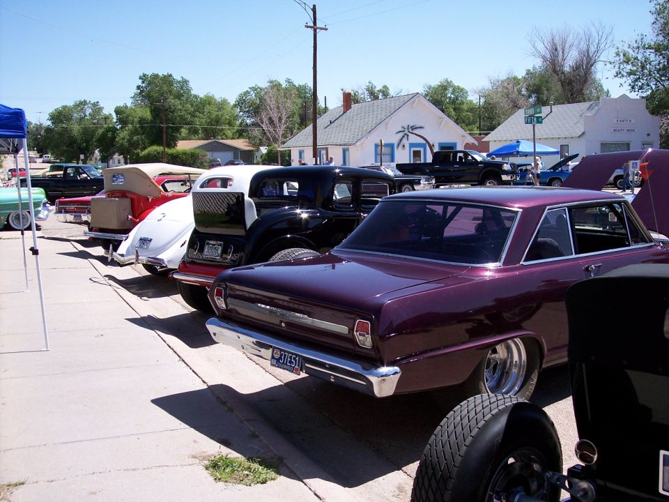 Several classic cars parked in a line on a sunny day, including a purple 1966 Chevrolet Nova