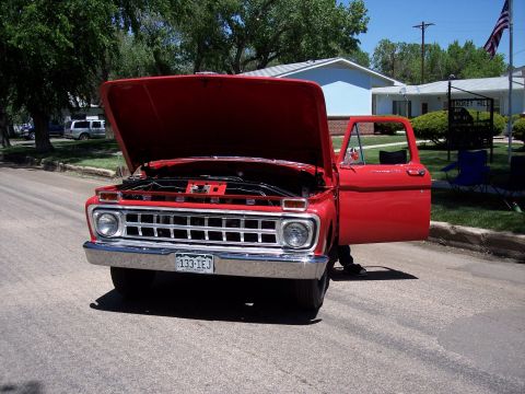 1972 Ford Ranchero - A red pickup truck is parked on a street with its hood and driver's door open, revealing the engine.