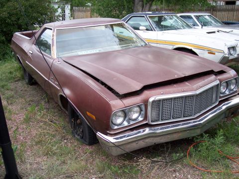 1972 Ford Ranchero - A weathered 1972 Ford Ranchero sits in a yard with its hood ajar and a flat front tire.