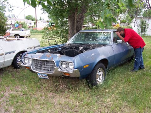 1972 Ford Ranchero - A blue 1972 Ford Ranchero sits in a grassy yard with its hood up, a man inspects the engine bay.