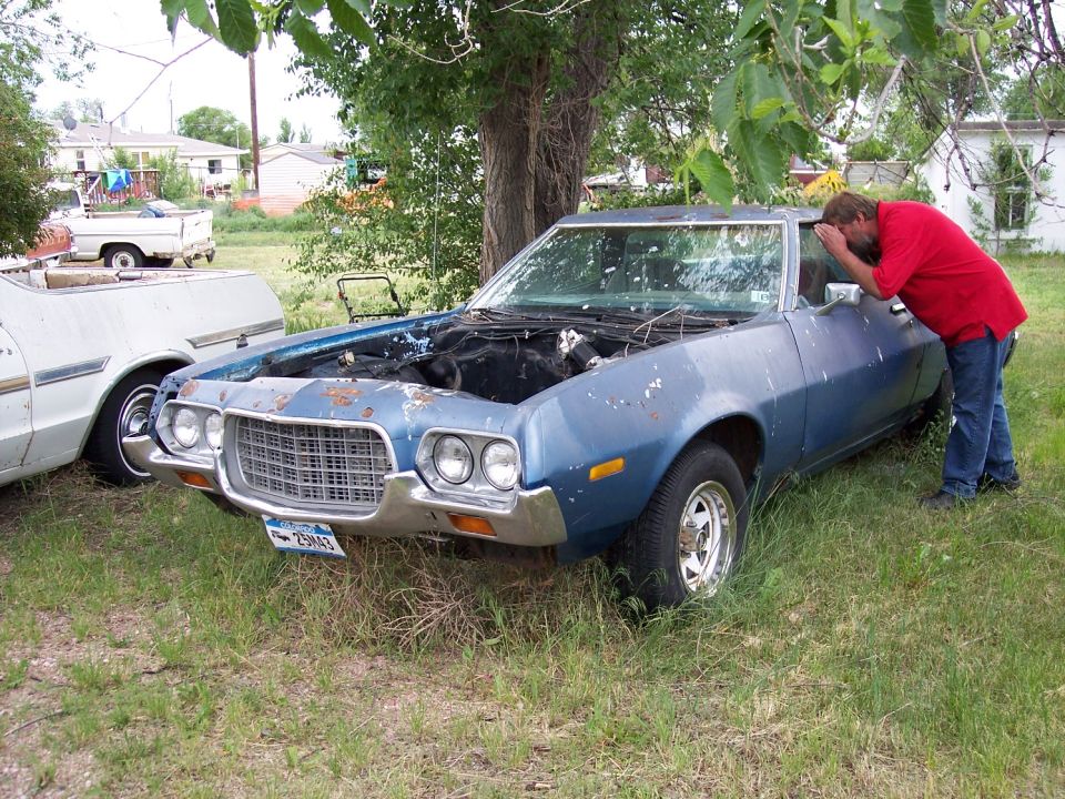 Blue 1972 Ford Ranchero parked in grass, hood open, man looking inside. Another vehicle partially visible to the left