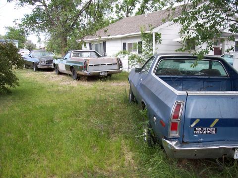 1972 Ford Ranchero - Three older model pickup trucks and a sedan are parked in a grassy yard next to a white house.