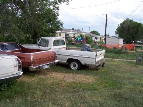 1972 Ford Ranchero - Two older model Ford trucks are parked in a yard under a cloudy sky.