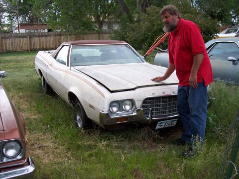 1972 Ford Ranchero - A man stands by a white 1972 Ford Ranchero with orange stripes, showing its front end and part of the bed.