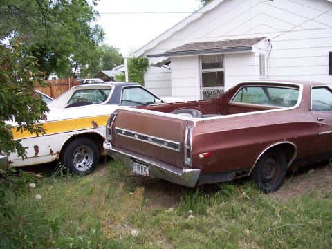 1972 Ford Ranchero - Two Ford Rancheros are parked in a grassy area next to a white house. The brown one is in the foreground.