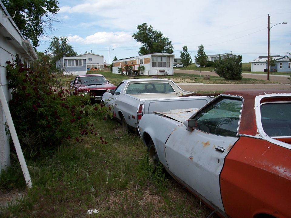 Two Ford Rancheros, one light gray and one red/gray, parked in grass next to a house