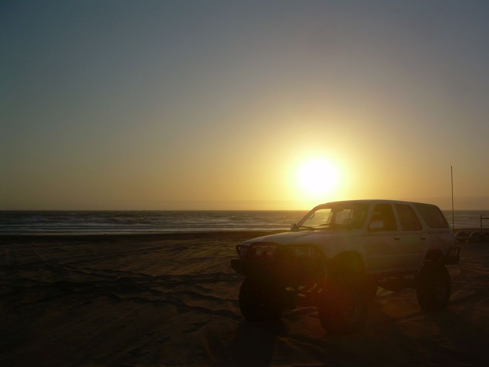 White 1993 Toyota 4Runner parked on a beach with the sun setting over the ocean