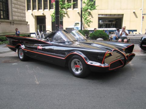 1991 Ford LTD Crown Victoria - Side three-quarter view of the black Batmobile with red trim and bat emblems parked on a downtown street.