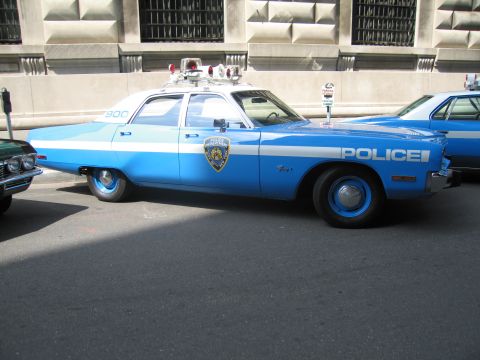 1991 Ford LTD Crown Victoria - two-tone blue vintage NYPD sedan with roof light bar parked curbside between other police cruisers.