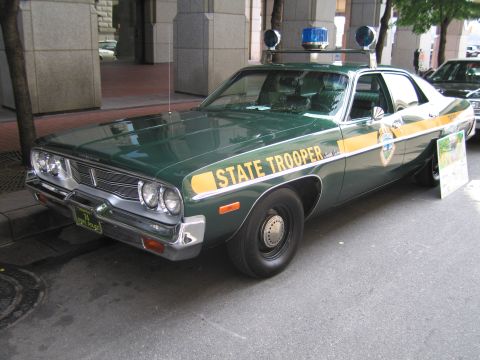 1991 Ford LTD Crown Victoria - vintage green-and-white State Trooper sedan with twin roof beacons and a gold side stripe parked beside a building.