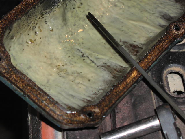 Rusty engine pan coated in milky tan oil sludge from coolant contamination