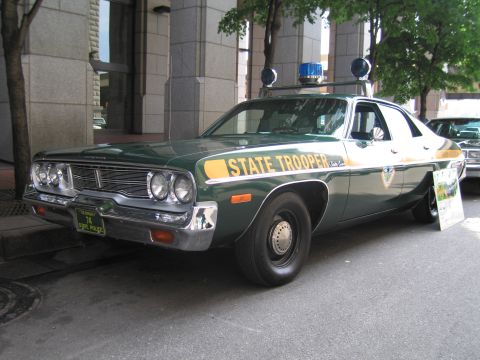 1991 Ford LTD Crown Victoria - Front three-quarter view of a green-and-white vintage State Trooper sedan with chrome bumper and roof beacons.