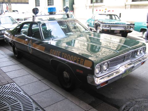 1991 Ford LTD Crown Victoria - Rear quarter of a green State Trooper sedan with three roof beacons, lined up with other classic patrol cars on a city street.