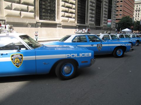 1991 Ford LTD Crown Victoria - row of light-blue-and-white Police Department sedans with shield decals and roof beacons lined up on the pavement.
