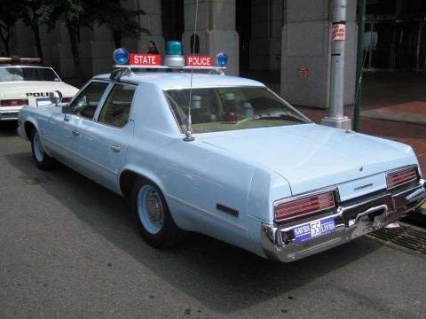 1991 Ford LTD Crown Victoria - Rear three-quarter view of a light-blue 1970s sedan topped with a STATE POLICE light bar parked on a city street.