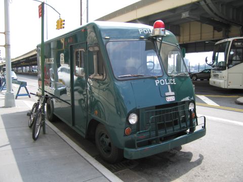 1991 Ford LTD Crown Victoria - green vintage POLICE step van with a single roof beacon parked at the curb with a bicycle leaning against it.