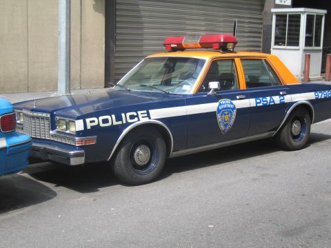 1991 Ford LTD Crown Victoria - navy-and-orange POLICE sedan marked PSA 2 9798 with a red roof light bar parked on a city street.
