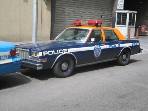 1991 Ford LTD Crown Victoria - navy-and-orange POLICE sedan marked PSA 2 9798 with red roof lights parked beside a light-blue cruiser.