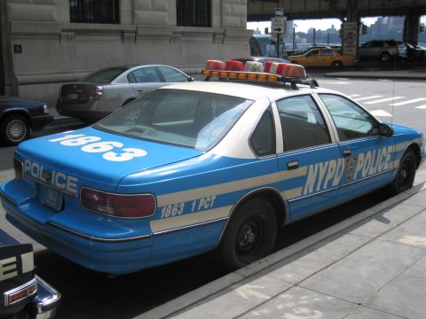 1991 Ford LTD Crown Victoria - Rear quarter view of a blue-and-white NYPD POLICE sedan marked 1863 1 PCT with a roof light bar parked curbside.