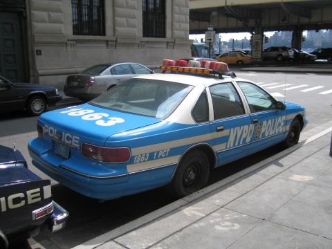 1991 Ford LTD Crown Victoria - Rear view of a blue-and-white NYPD POLICE sedan numbered 1863 1 PCT parked near an elevated roadway with a taxi behind.