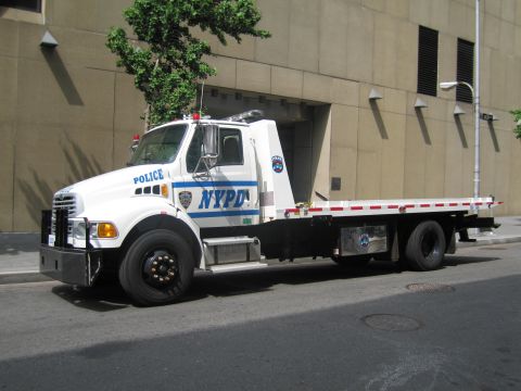 1991 Ford LTD Crown Victoria - Side profile of a white NYPD flatbed tow truck with blue NYPD lettering and roof beacons parked on a city street.