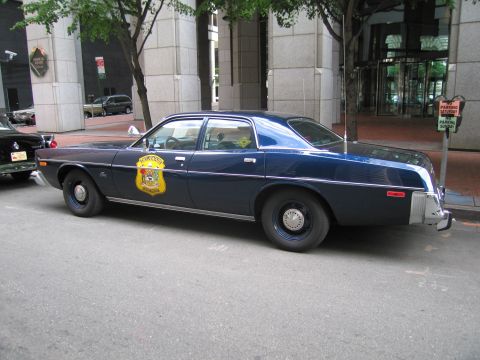 1991 Ford LTD Crown Victoria - dark blue four-door vintage police sedan bearing a gold state agency shield on the door is parked along a downtown curb.