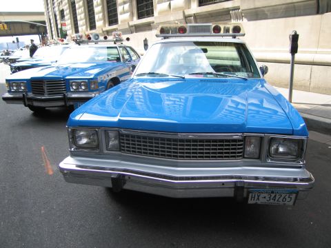 1991 Ford LTD Crown Victoria - Front view of a blue vintage police car with rooftop lights and a New York plate reading HX-34265, parked among other patrol cars.