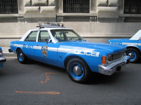 1991 Ford LTD Crown Victoria - blue-and-white NYPD 60th Precinct sedan with rooftop lightbar and POLICE lettering sits curbside by a stone building.