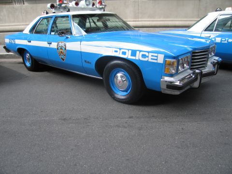 1991 Ford LTD Crown Victoria - blue-and-white vintage NYPD sedan with rooftop emergency lights and POLICE on the fender, photographed front-three-quarter.