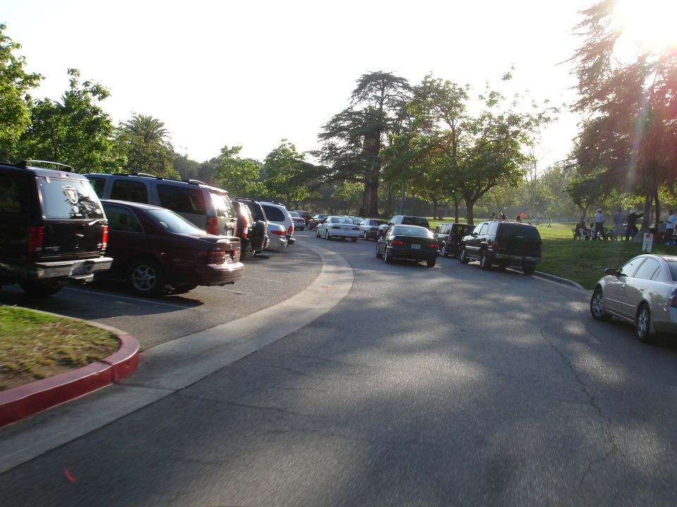 Cars parked on a curved road in a park with people in the background
