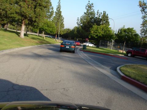 1993 Ford Taurus - Several cars drive along a paved road in a park-like setting with trees and grass.