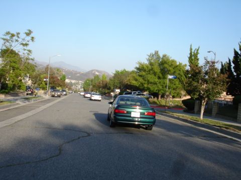 1993 Ford Taurus - A green sedan drives down a residential street on a clear day, with other vehicles and houses visible.