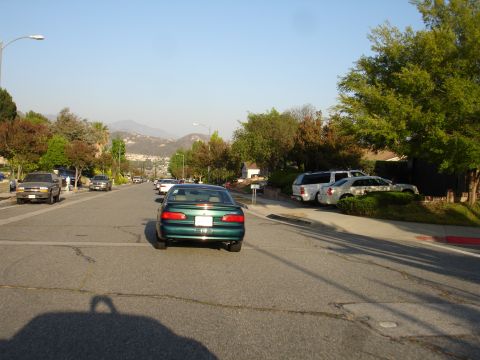 1993 Ford Taurus - A green sedan is seen from the rear on a residential street with other vehicles parked on the side.