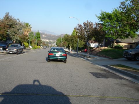 1993 Ford Taurus - A green sedan is seen from behind driving down a residential street with parked cars and houses.