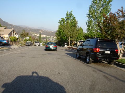 1993 Ford Taurus - Residential street with several cars and SUVs parked and driving under a clear sky.