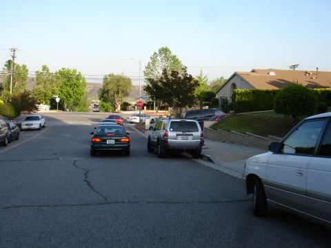 1993 Ford Taurus - A dark sedan is seen from the rear, driving down a residential street with several other vehicles present.