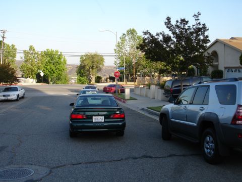 1993 Ford Taurus - A 1993 Ford Taurus is seen from the rear on a residential street, with other vehicles and homes visible.