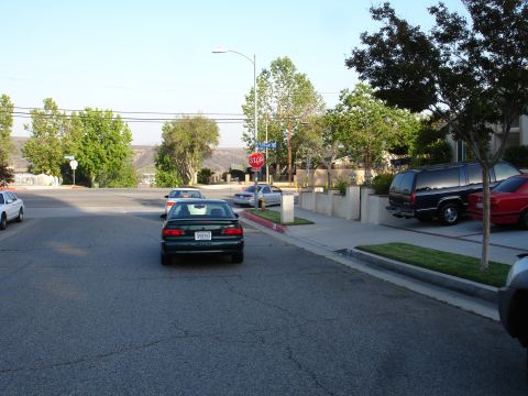 1993 Ford Taurus - A dark green sedan is seen from the rear on a residential street with a stop sign and other vehicles present.