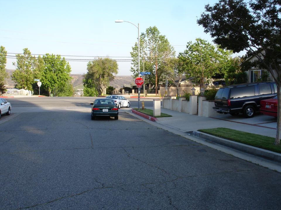Dark green sedan driving on a street with a black SUV parked on the side