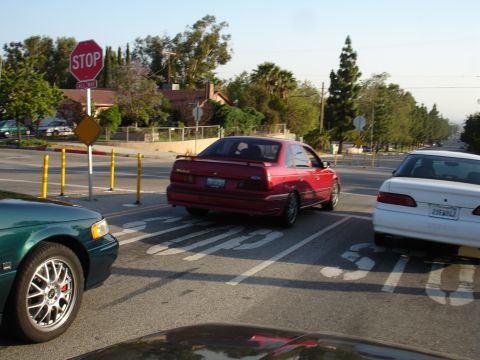 1993 Ford Taurus - Red 1993 Ford Taurus sedan at a stop sign, with other vehicles present.