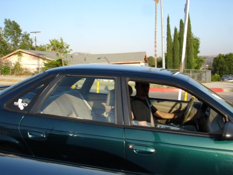 1993 Ford Taurus - A driver is seen from the side in a green sedan with a sticker on the rear window.