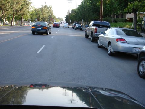 1993 Ford Taurus - A view from a car driving down a street with multiple vehicles in traffic and parked along the curb.