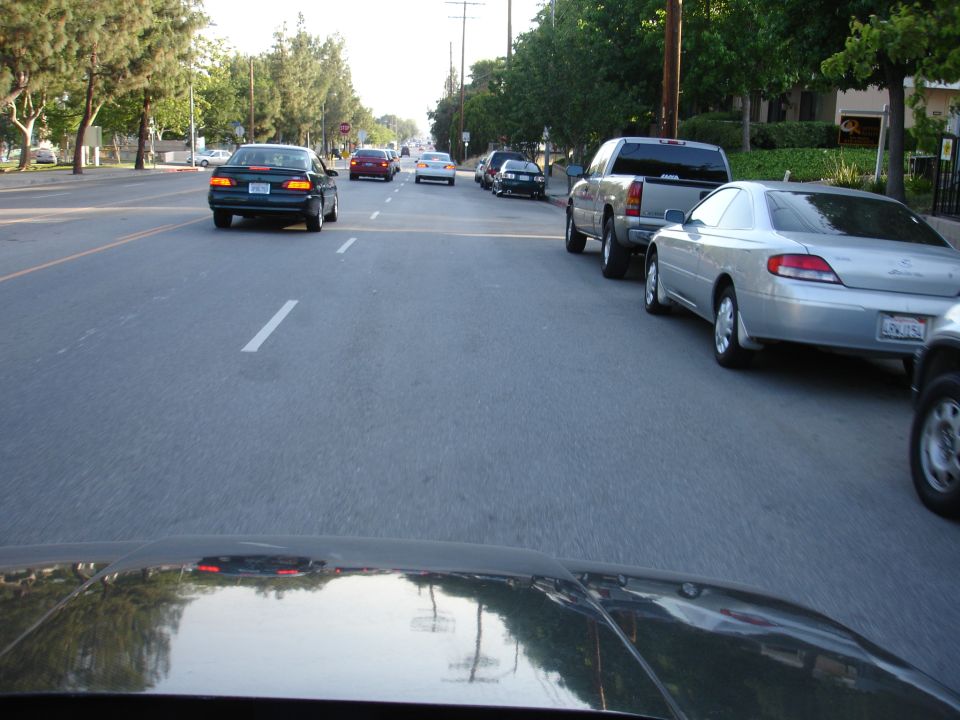 Cars driving down a street, some parked on the side