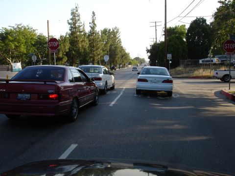 1993 Ford Taurus - A red 1993 Ford Taurus sedan with a spoiler is seen from the rear, stopped at a traffic light.