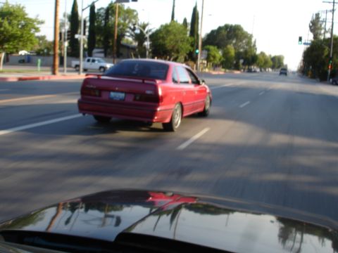 1993 Ford Taurus - A red sedan is captured from behind as it drives down a suburban street.