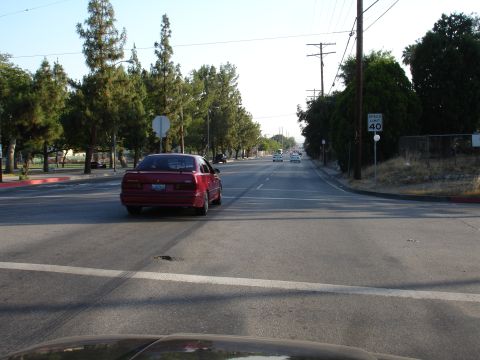 1993 Ford Taurus - A red sedan is seen from behind as it drives down a street with multiple other vehicles in the distance.