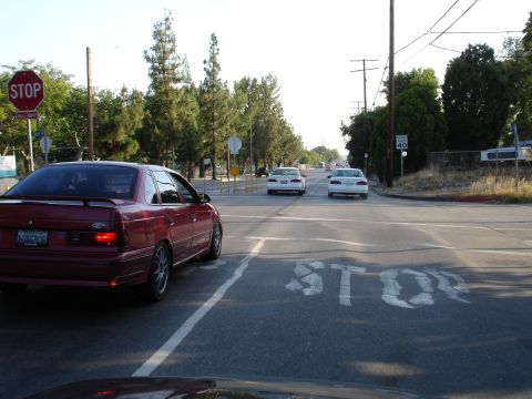 1993 Ford Taurus - Red 1993 Ford Taurus sedan at a stop sign intersection with other cars visible.