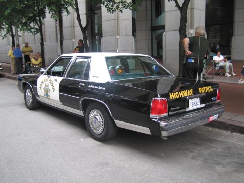 1991 Ford LTD Crown Victoria - Rear three-quarter of a black-and-white Ford Highway Patrol sedan with HIGHWAY PATROL lettering across the trunk, parked curbside.